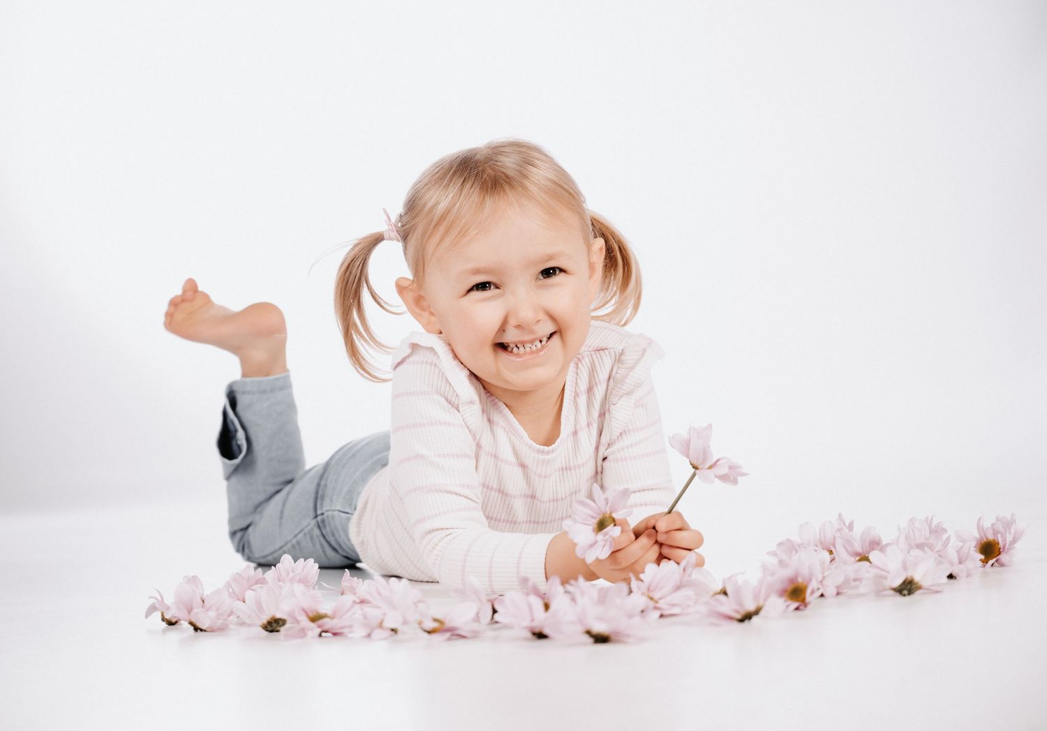 Mädchen liegt auf dem Studio-Boden in Gelsenkirchen-Hassel hält eine  Blume in der Hand und lächelt zwischen verstreuten Blütenblättern.