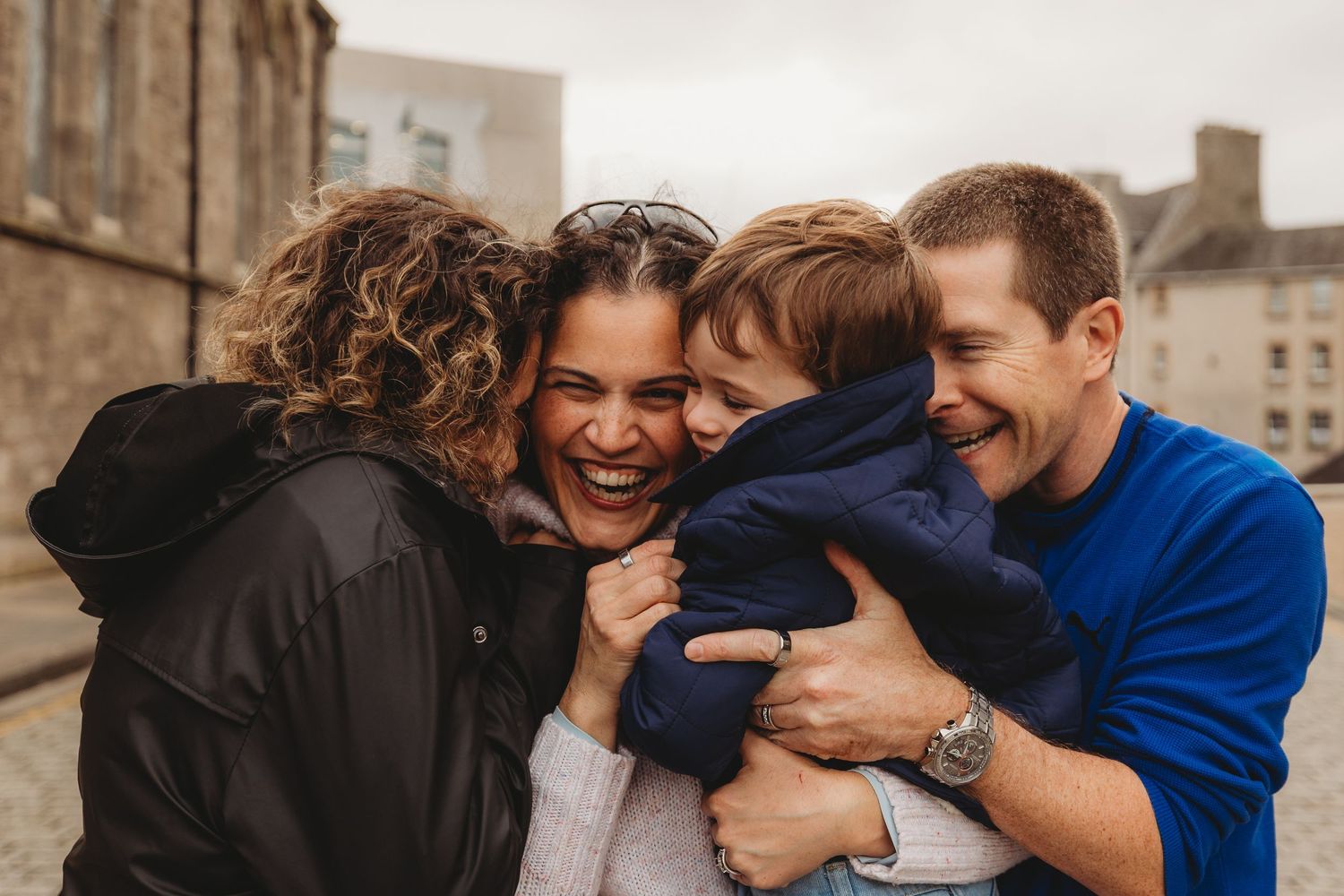 A group of friends laugh and embrace while standing together outdoors on a cloudy day.