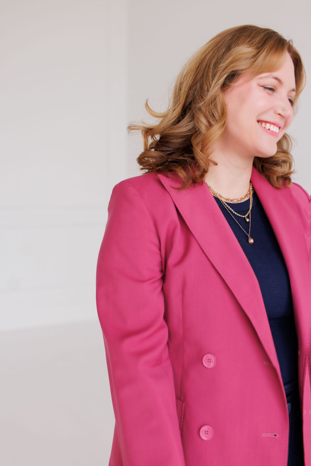 A professional wearing a bright pink blazer and navy top smiles warmly while posing against a light background.