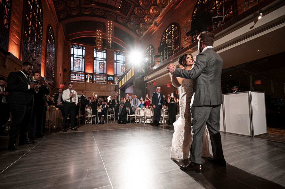 A couple dances elegantly in a grand ballroom with dramatic lighting and architectural details in the background.