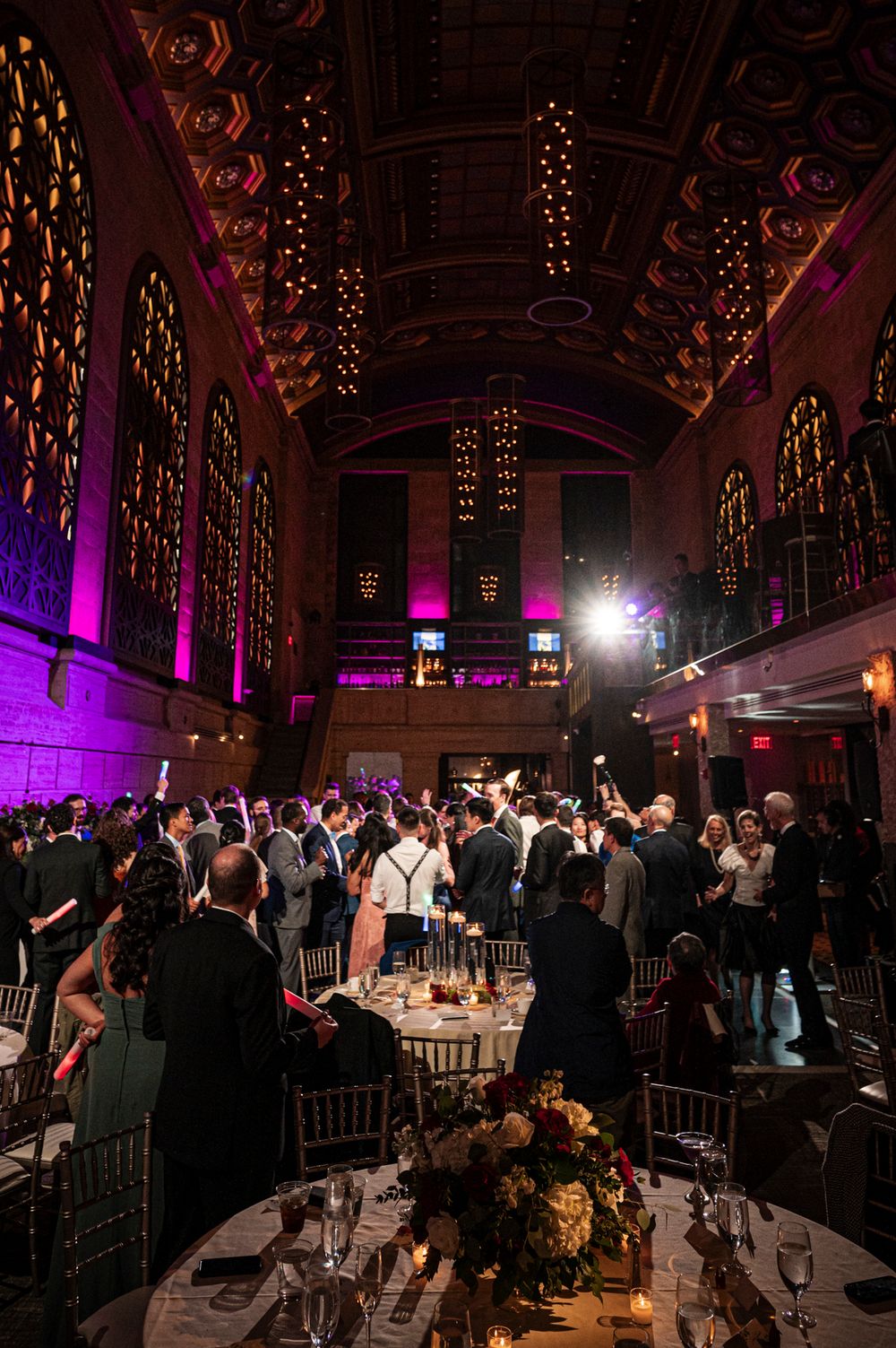 Wedding reception venue with elegant lighting and guests mingling in a grand ballroom decorated with purple uplighting.