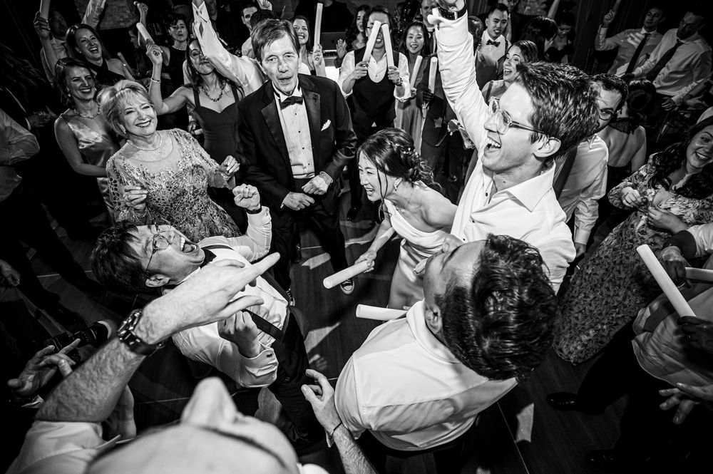 Black and white photo of a lively dance floor at a wedding reception with guests dancing and celebrating.