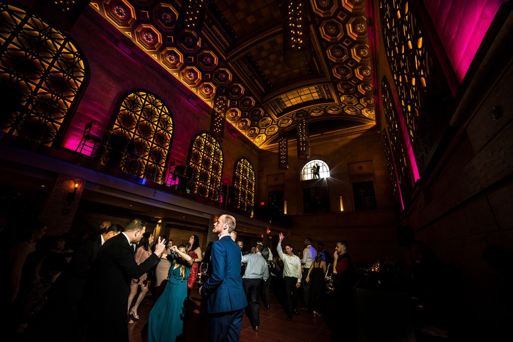 Guests dancing in Union Trust in Philadelphia with dramatic architectural details and pink-purple mood lighting.