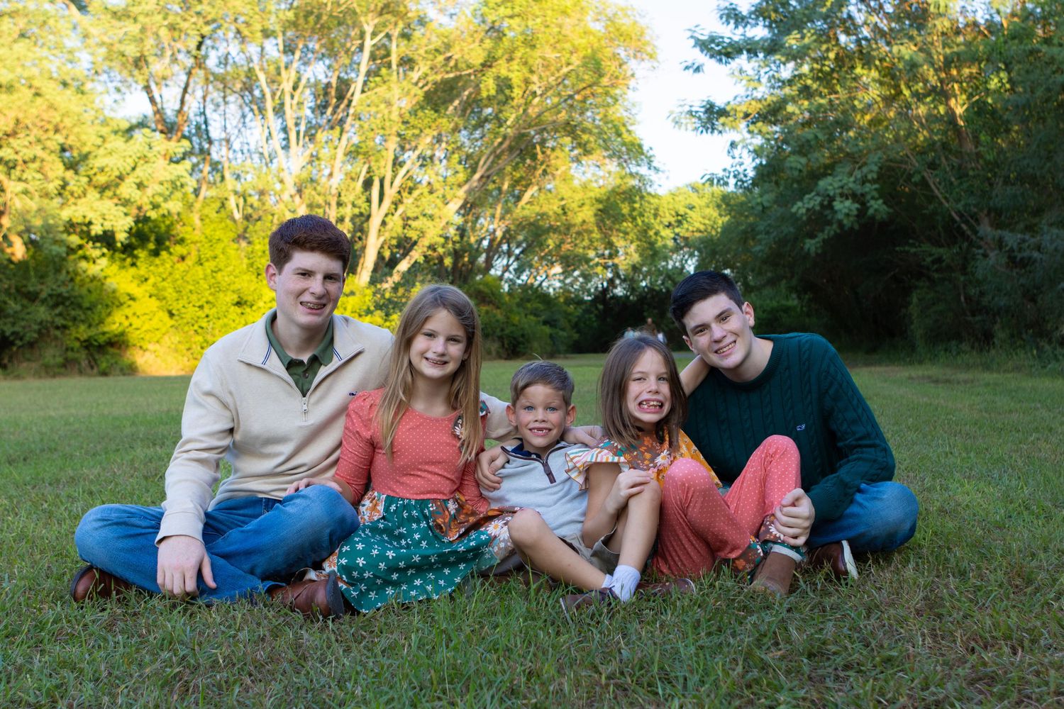 A group sits together on grass during a sunny autumn day with golden trees in the background.