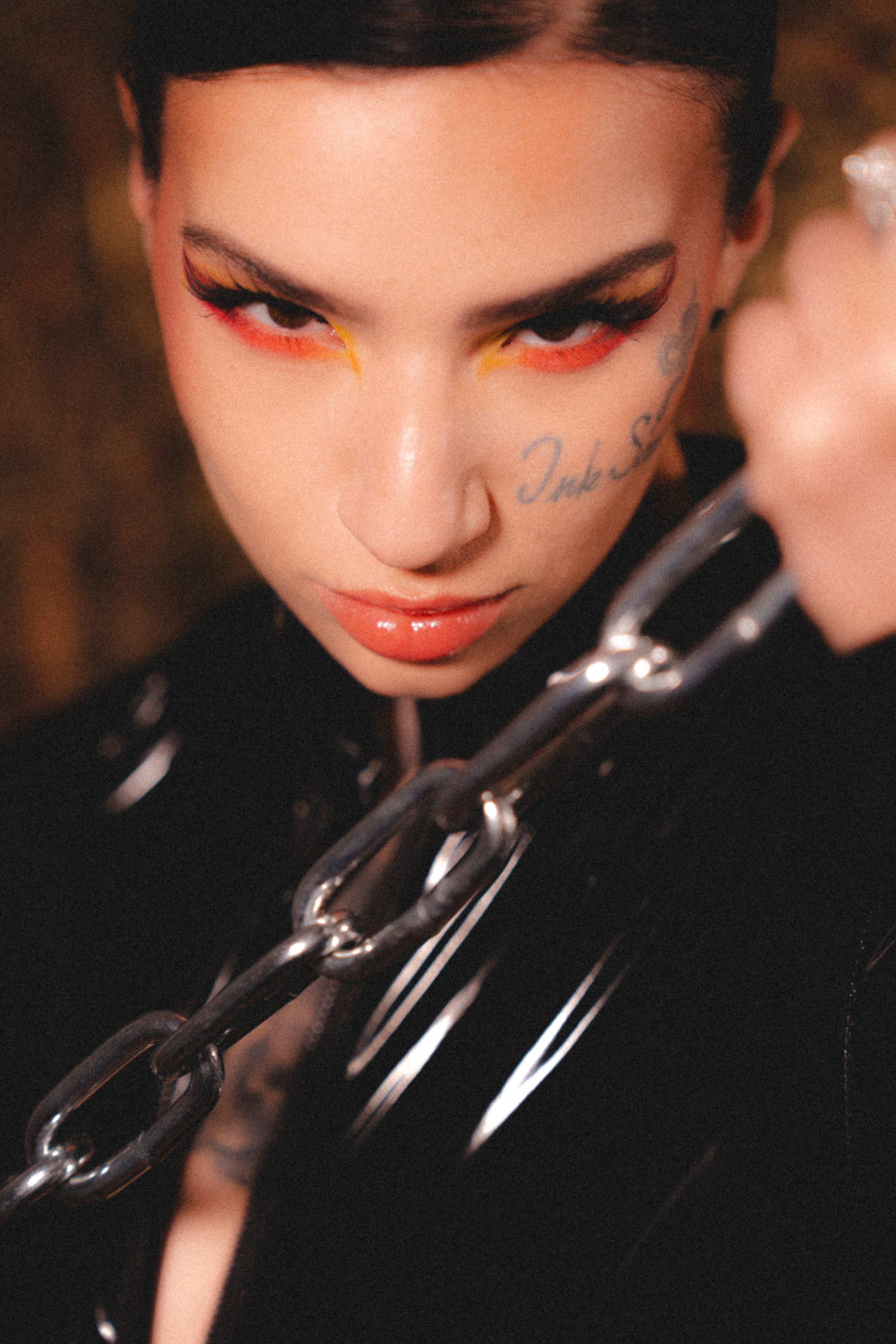 Dramatic portrait with bold red eye makeup and black chain accessory.