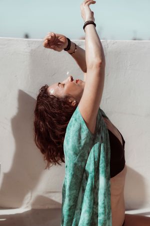 Dynamic pose of dancer in turquoise fabric against white wall.