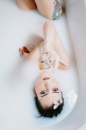 Artistic portrait series of a person floating in milky white water with butterfly decorations and dark hair.