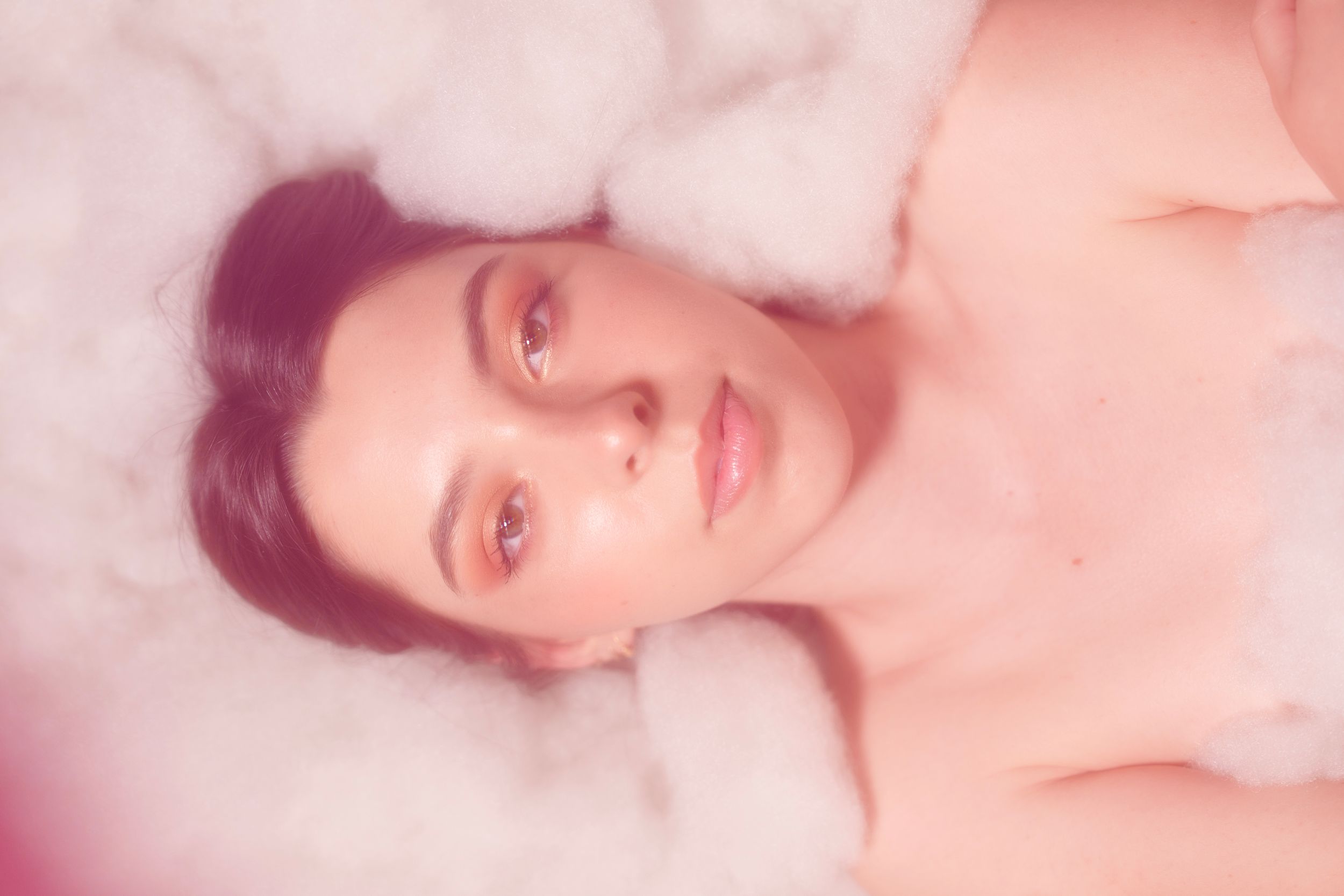 Dreamy ethereal portrait with soft pink hue and white cotton clouds creating romantic atmosphere.