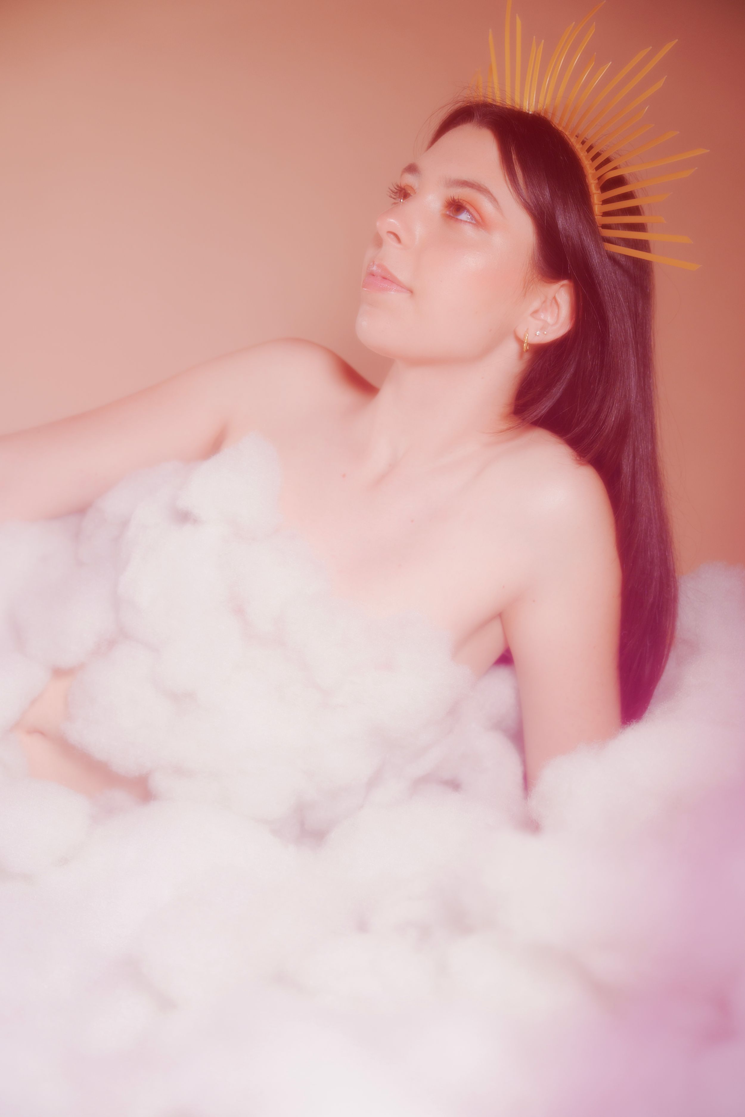 Ethereal portrait of someone lying in pink-tinted clouds with a golden crown effect.