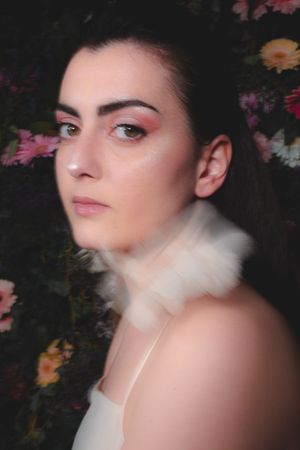 Ethereal portrait with floral background and white fur collar detail.