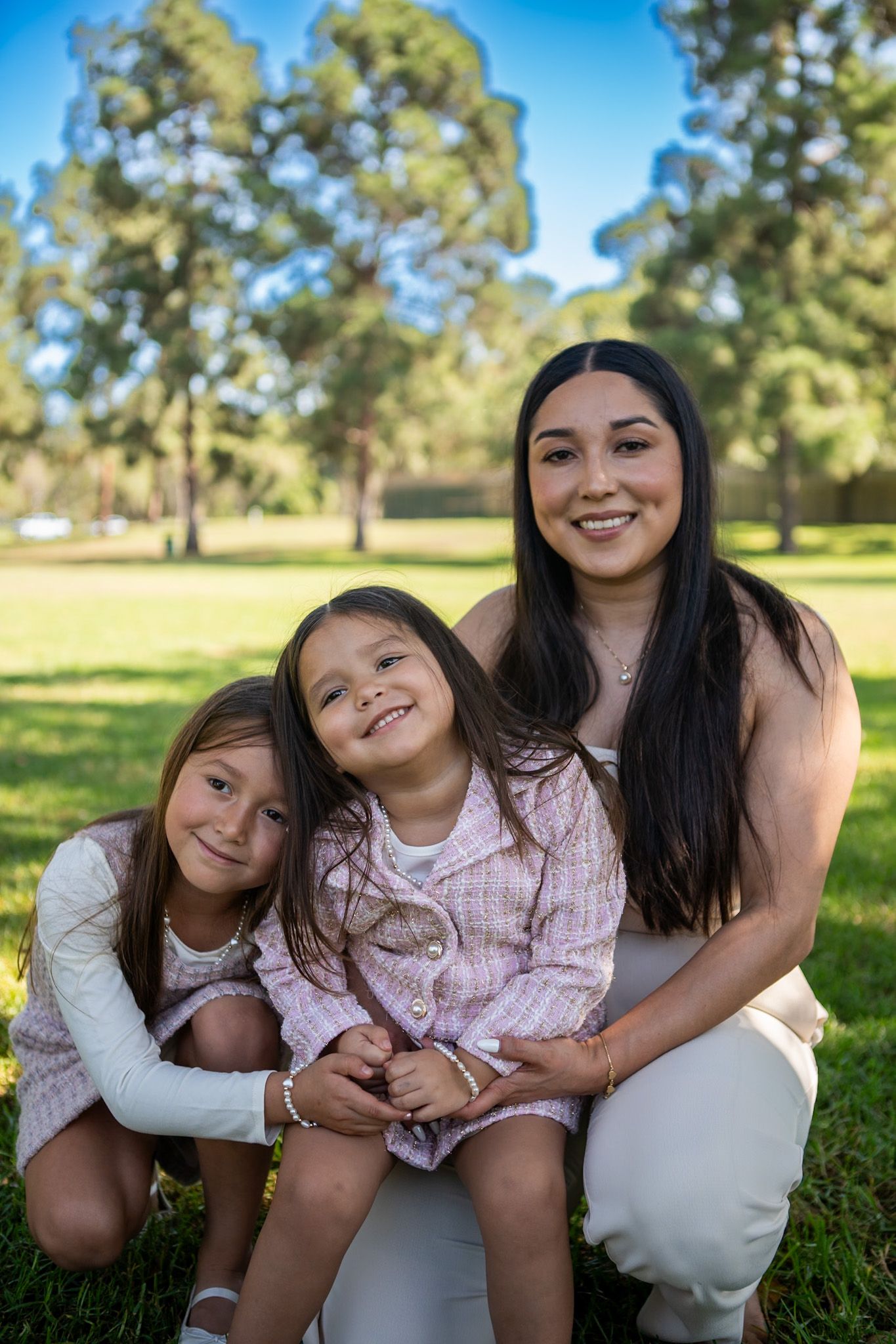 A playful outdoor photoshoot in a sunny park with people embracing and smiling on the grass.