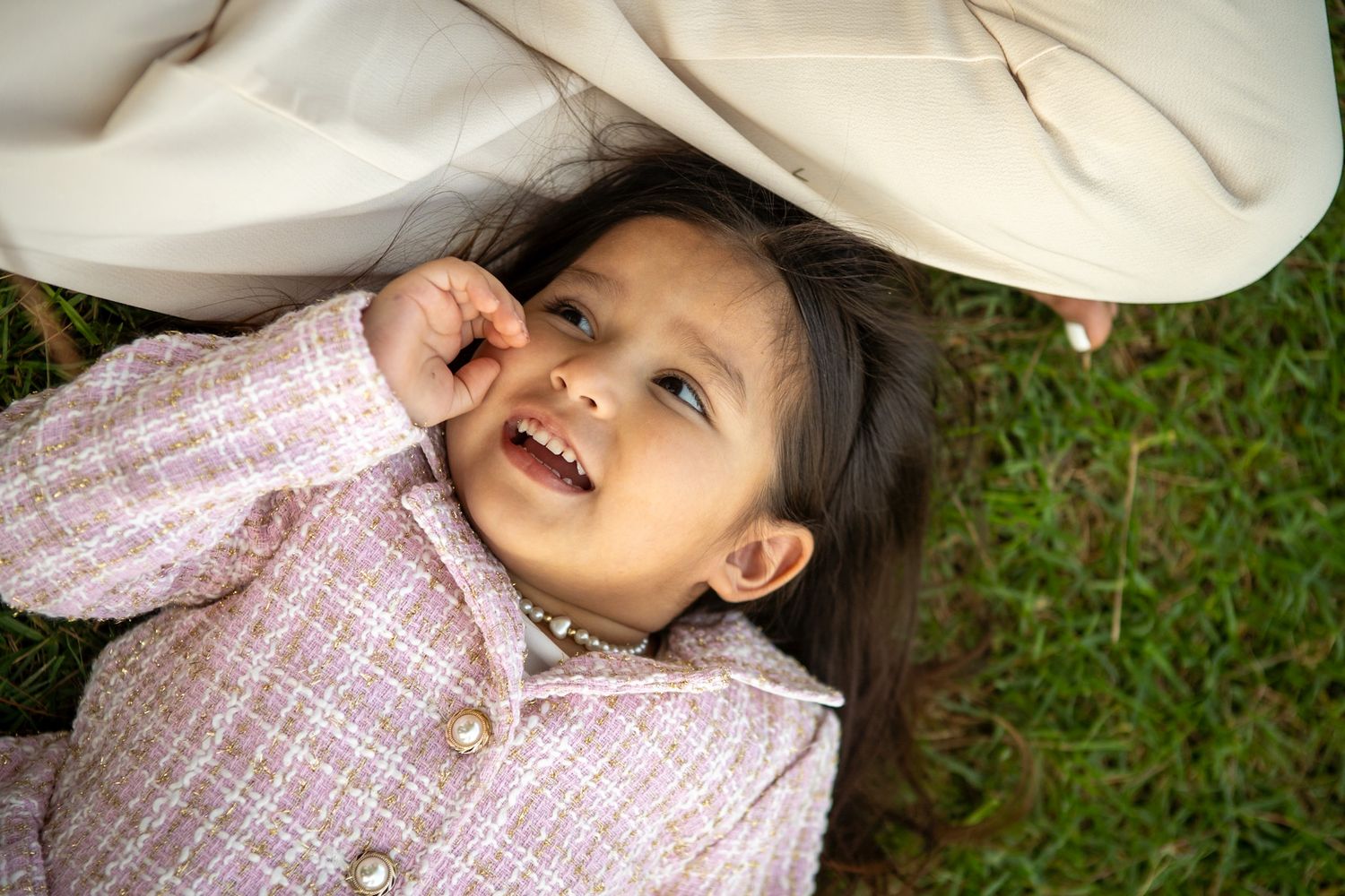 A sequence of candid photos showing someone lying in grass wearing a pink and white checkered dress.