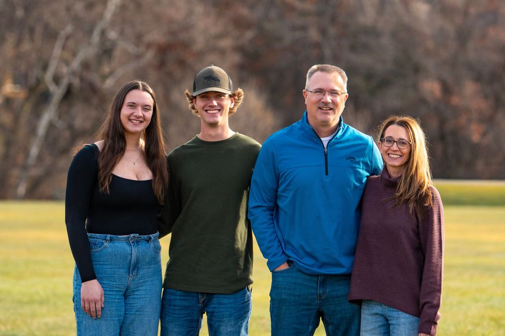 A family group poses together outdoors wearing coordinated blue and burgundy outfits.