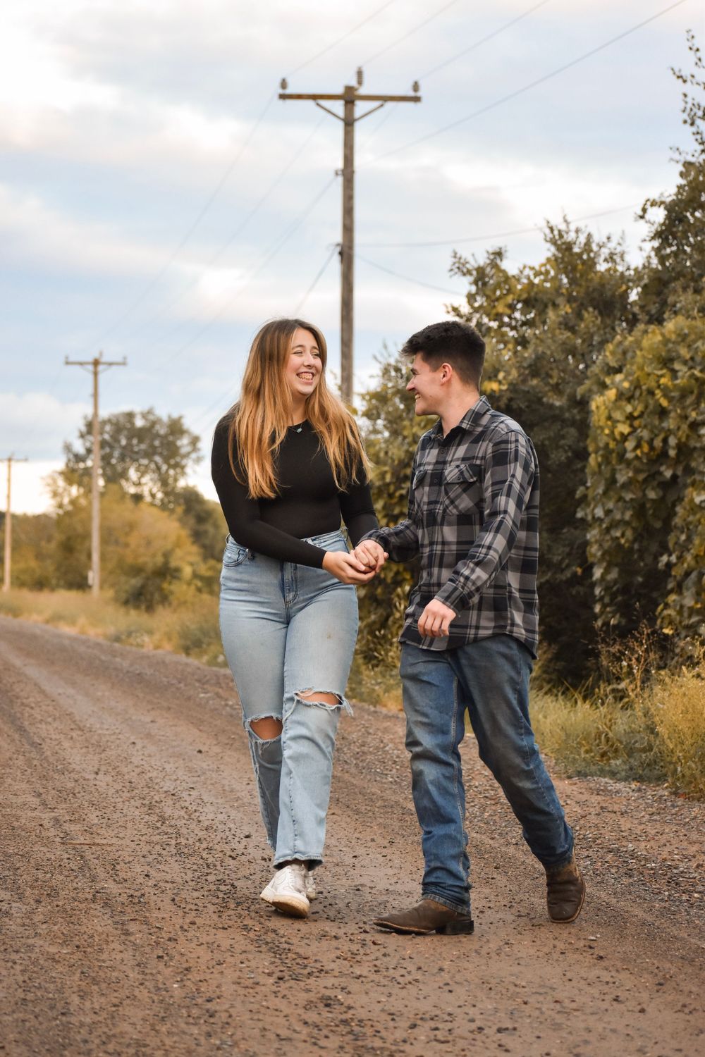 A couple shares playful moments together on a dirt road during sunset with utility poles in the background.