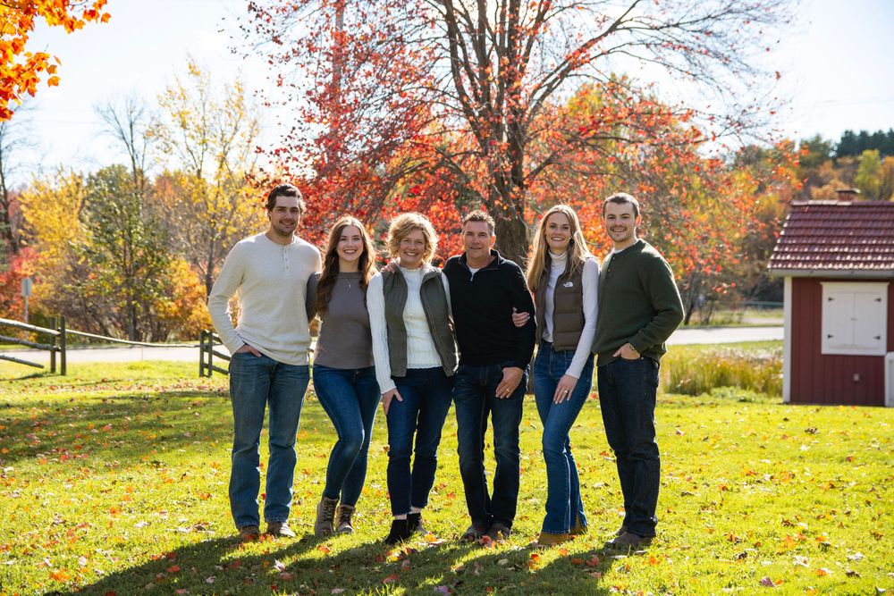 Large family group posing together outdoors during fall with colorful autumn trees in background.