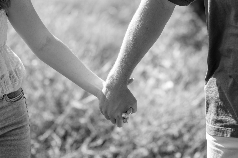 Close-up shot of hands holding each other tenderly in black and white.