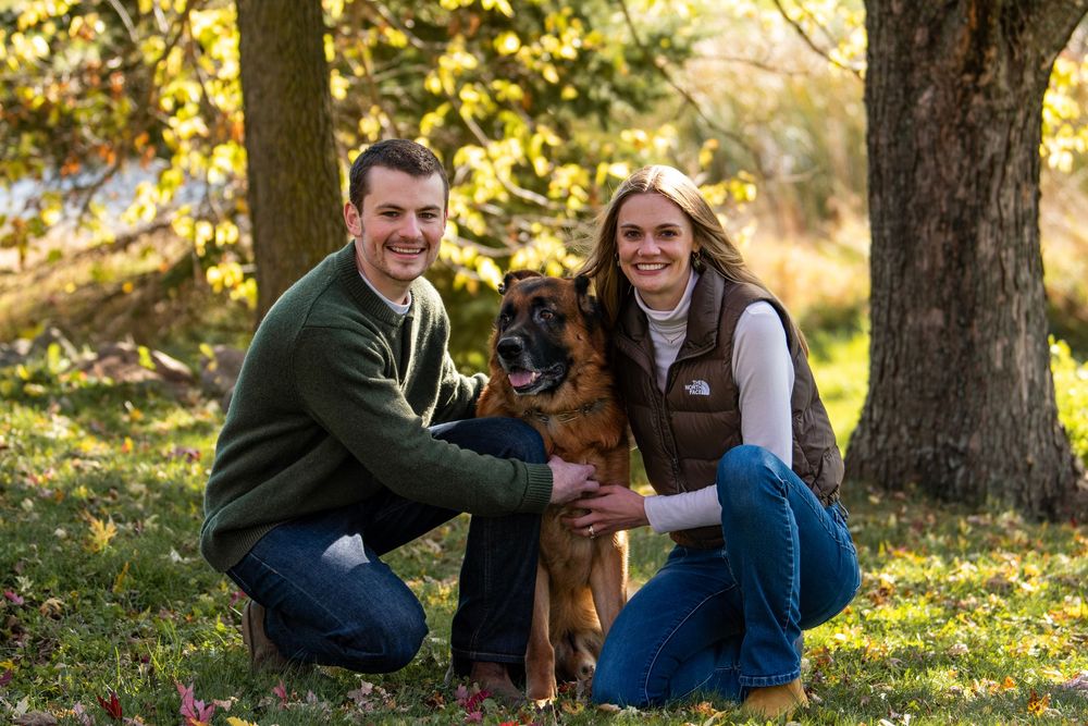 Family and dog playing together in autumn park with golden sunlight filtering through trees.