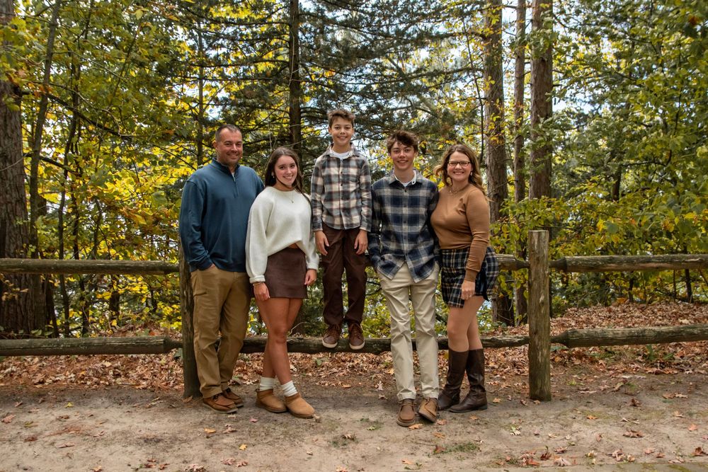 A group poses together for photos in a wooded outdoor setting during autumn.