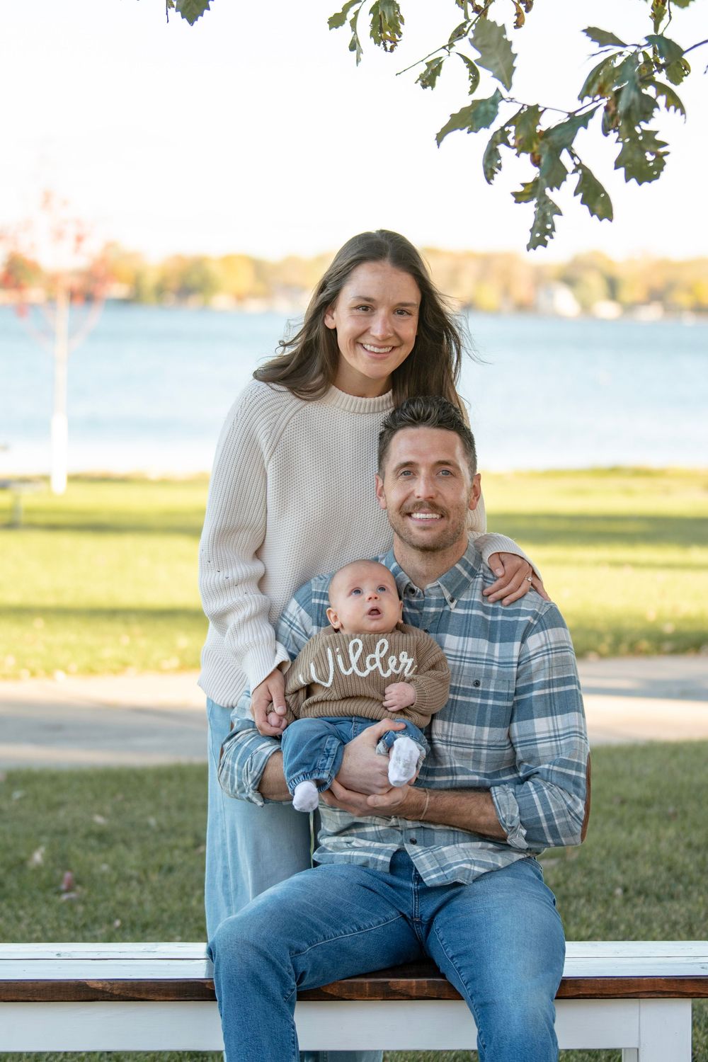 Family relaxing together on white bench near waterfront during golden hour.