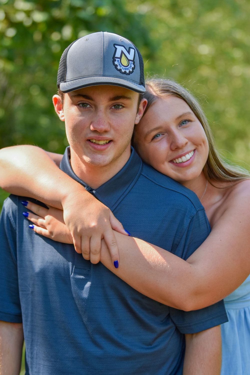 A couple shares affectionate embraces outdoors against a green natural background.
