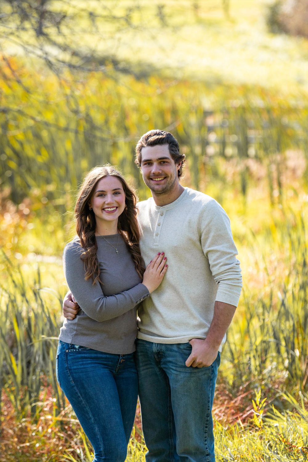 Couple laughing together in golden field during sunset photoshoot.