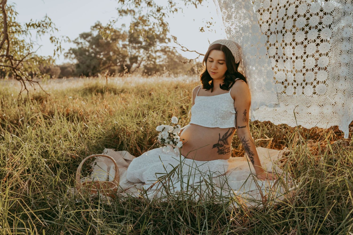 Expectant mother sitting in golden grass during an outdoor maternity photography session at sunset.