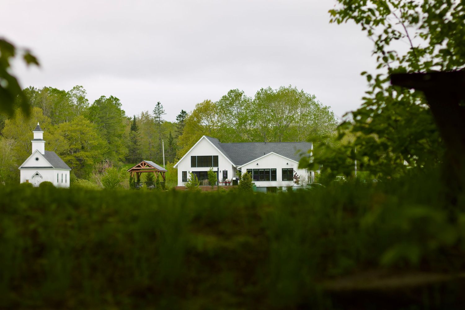 A white, single-level home and white church with a grassy foreground