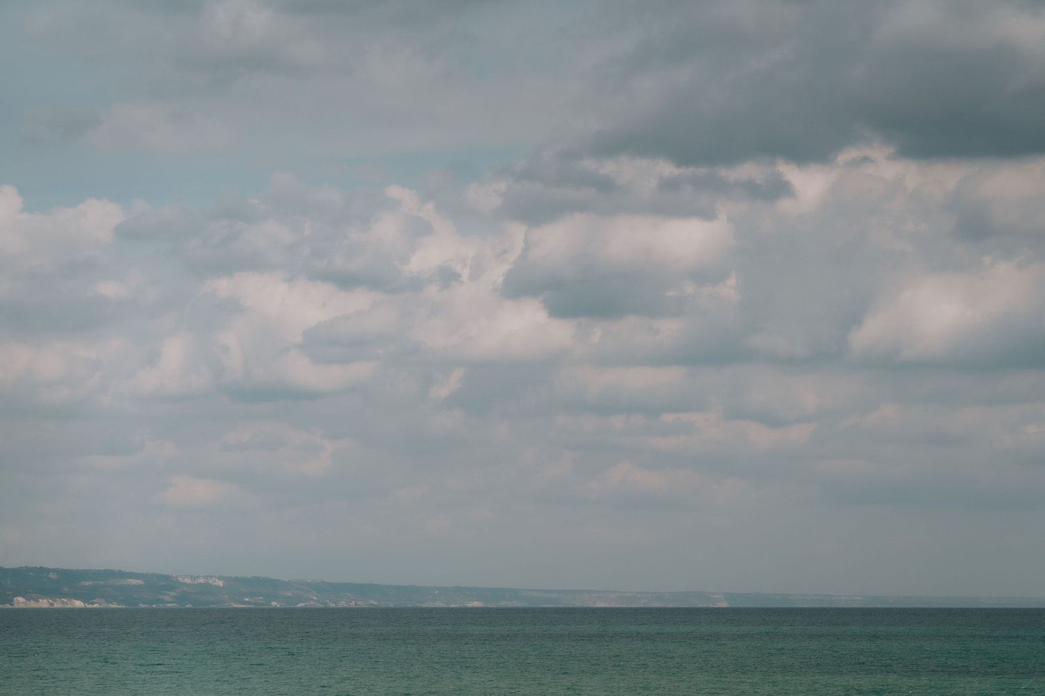 Calm turquoise sea under a dramatic cloudy sky with distant coastline visible on the horizon.