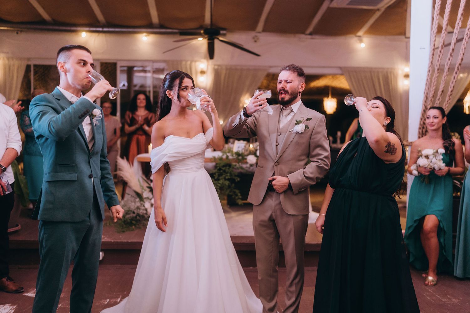 Bride and groom toast with wedding party guests in elegant green-themed reception venue during celebration.