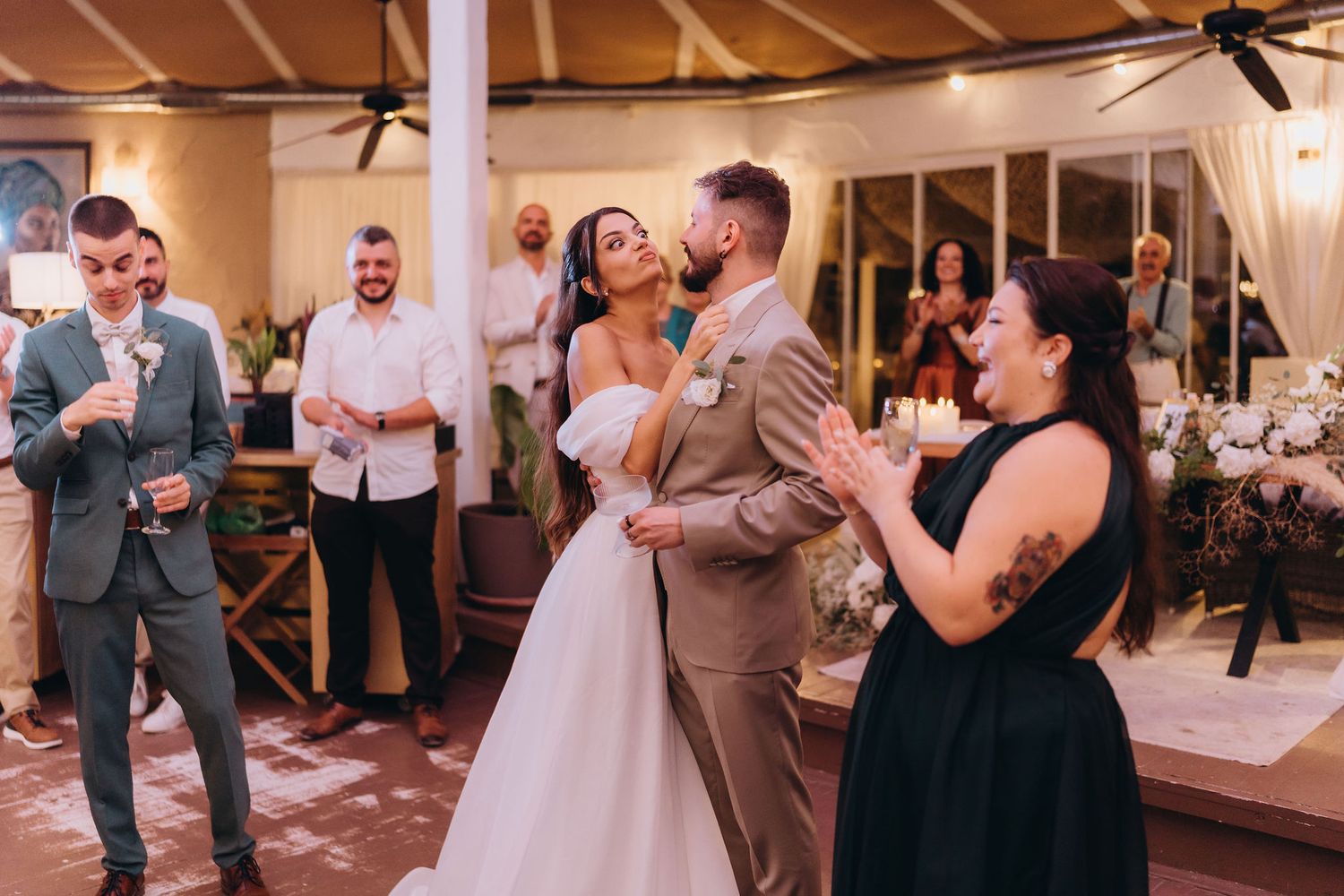 Bride and groom share first dance at wedding reception while guests clap and celebrate around them.