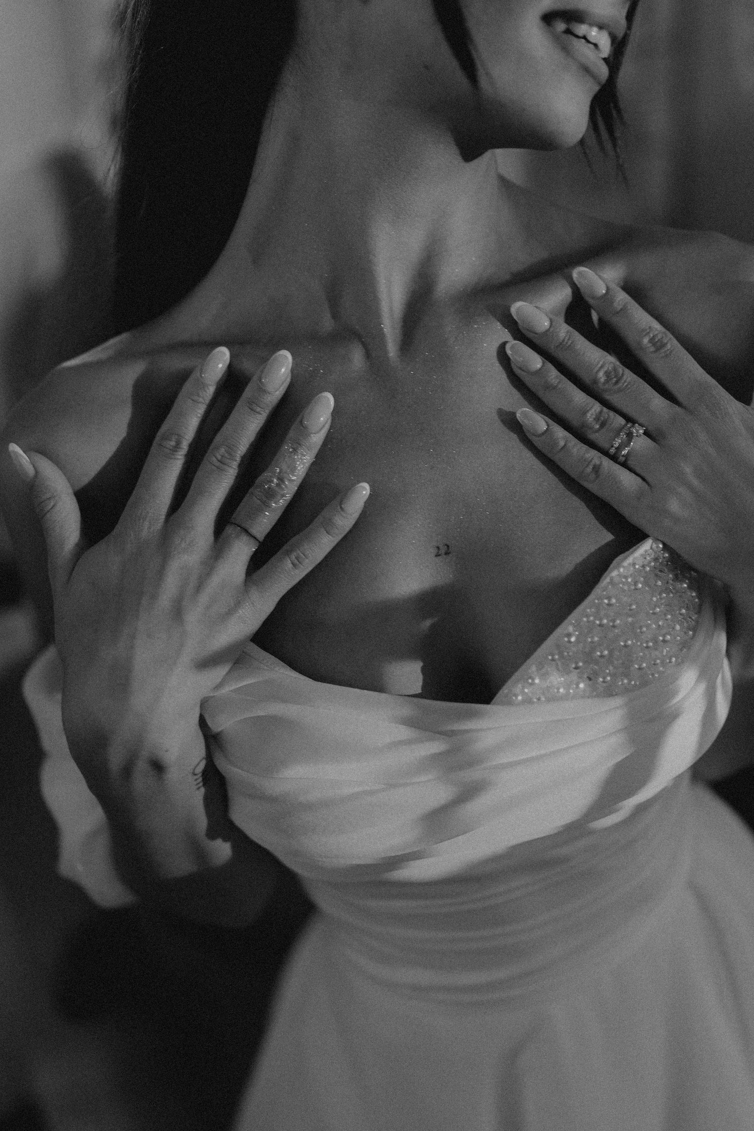 Black and white photo of a bride in a strapless wedding gown with hands placed on her chest, smiling softly.