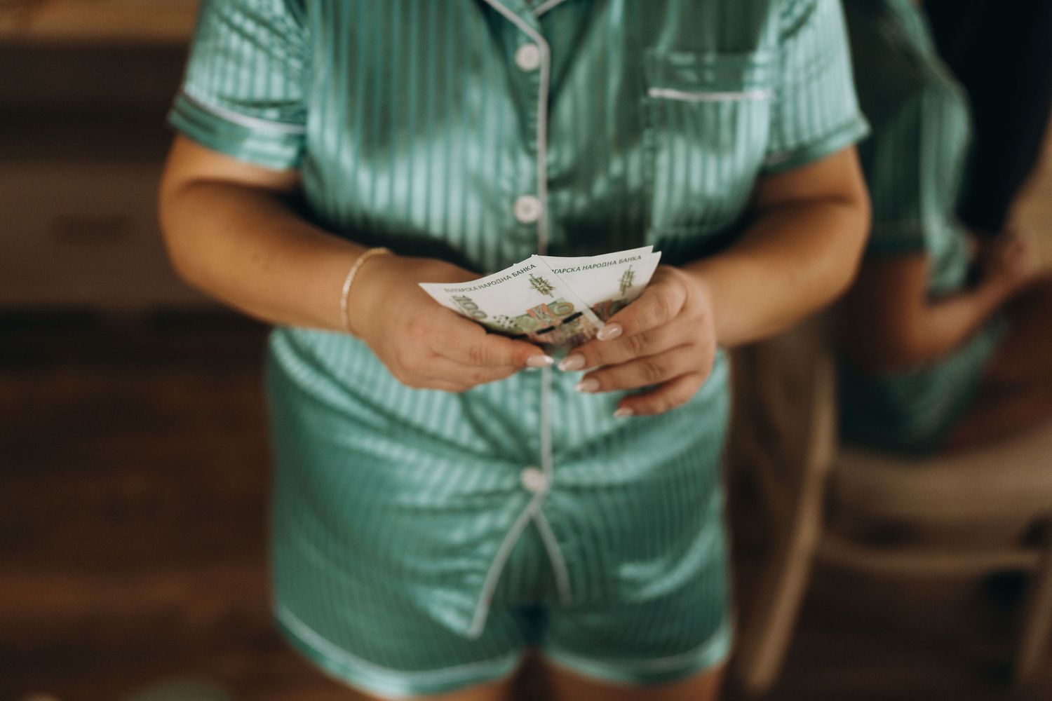 Child in teal satin pajamas counting money, holding US dollar bills with a bracelet on wrist.