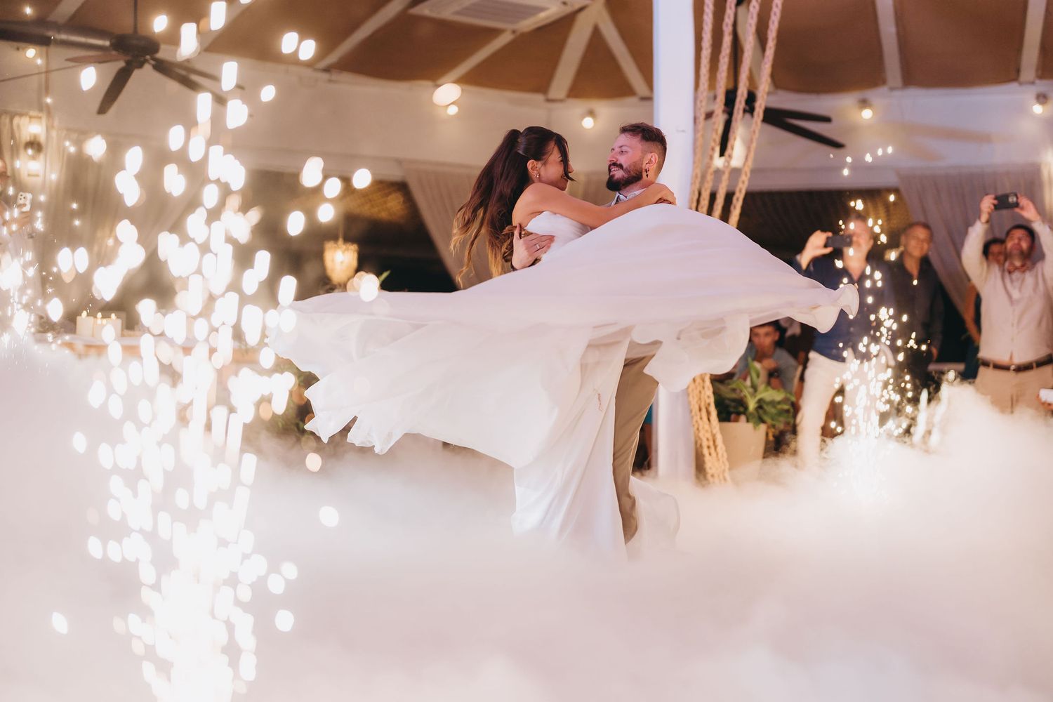Bride and groom share first dance surrounded by sparkling fireworks and dramatic fog on their wedding night.