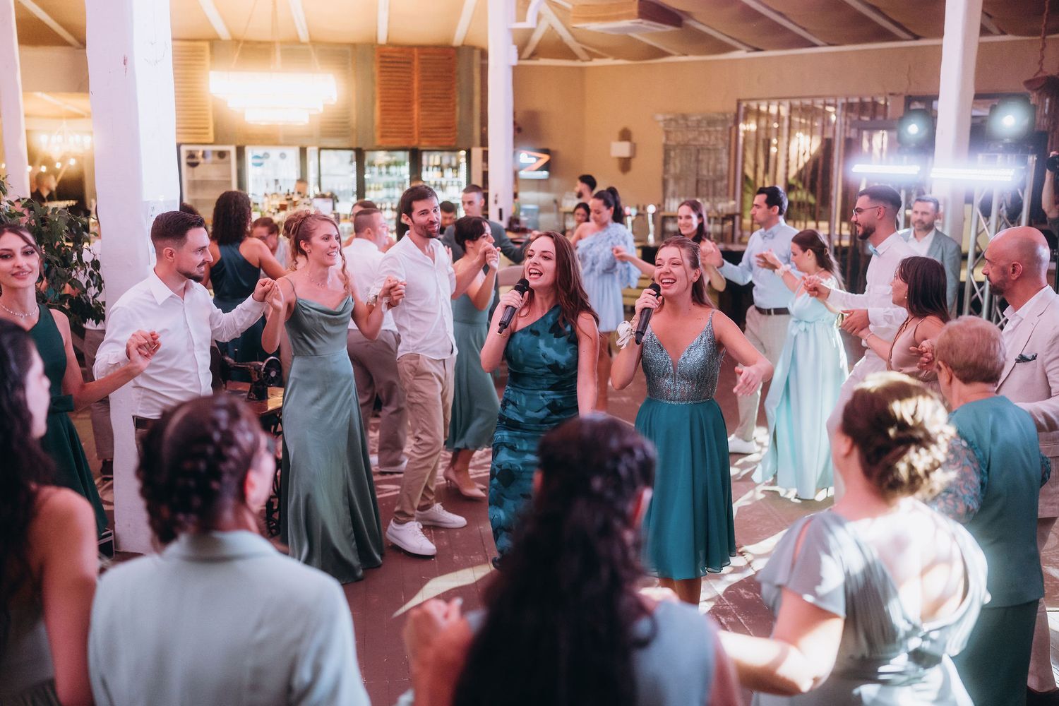 Guests in elegant attire dancing joyfully at a wedding reception in a warmly lit venue.