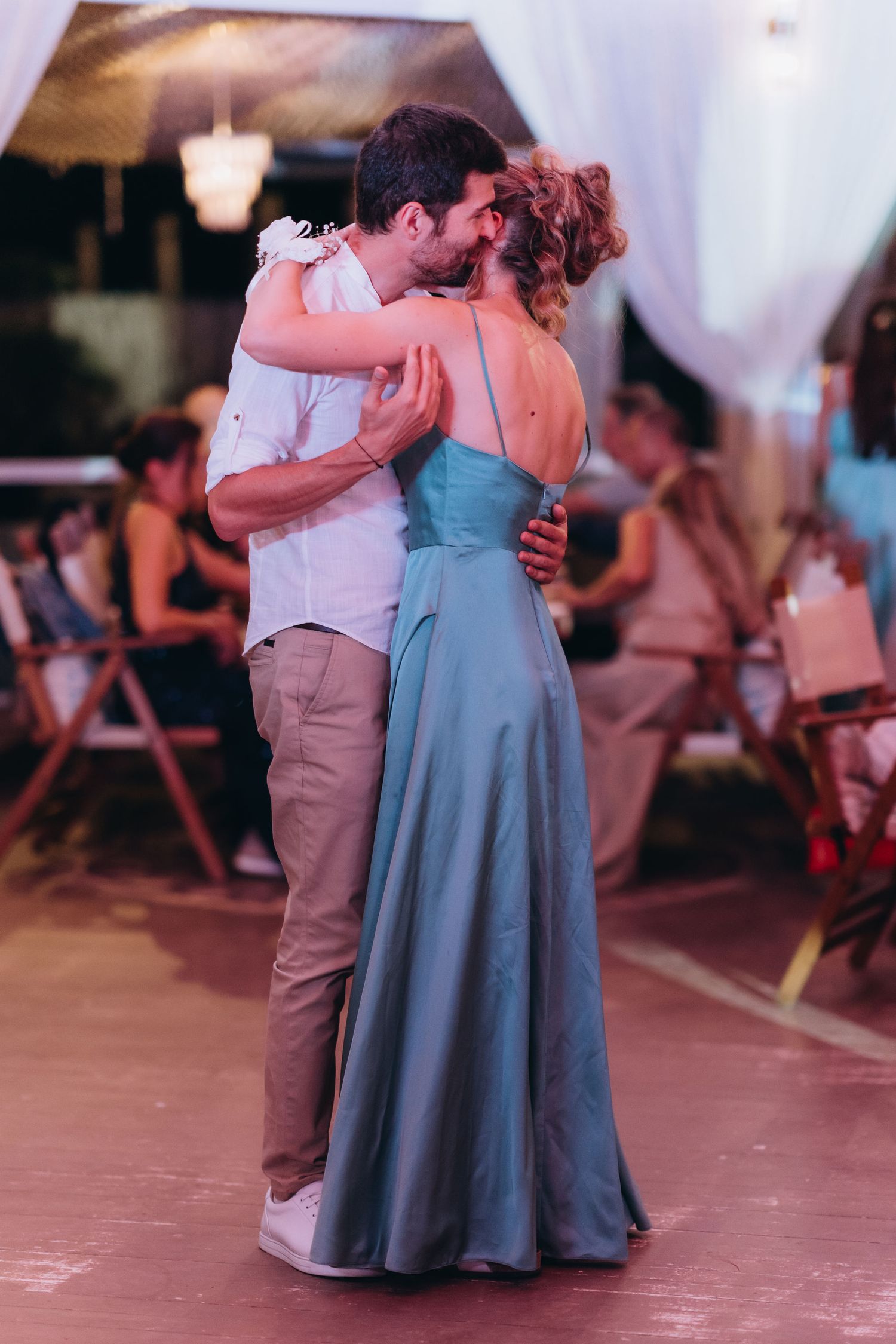 Couple sharing a romantic first dance at a wedding reception, woman in elegant teal gown, evening celebration.