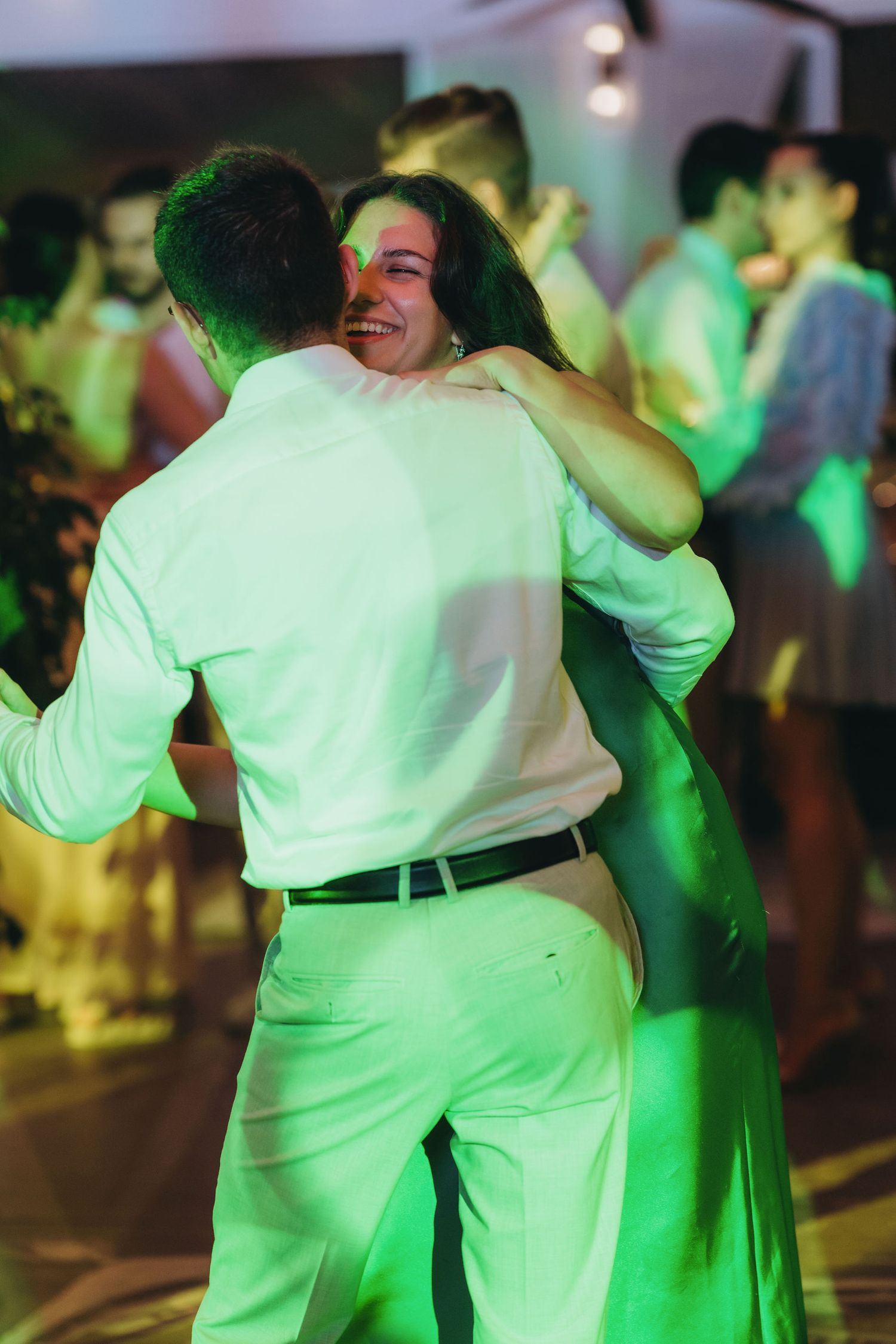 Couple embracing and dancing joyfully on a dance floor bathed in green light at a festive evening event.