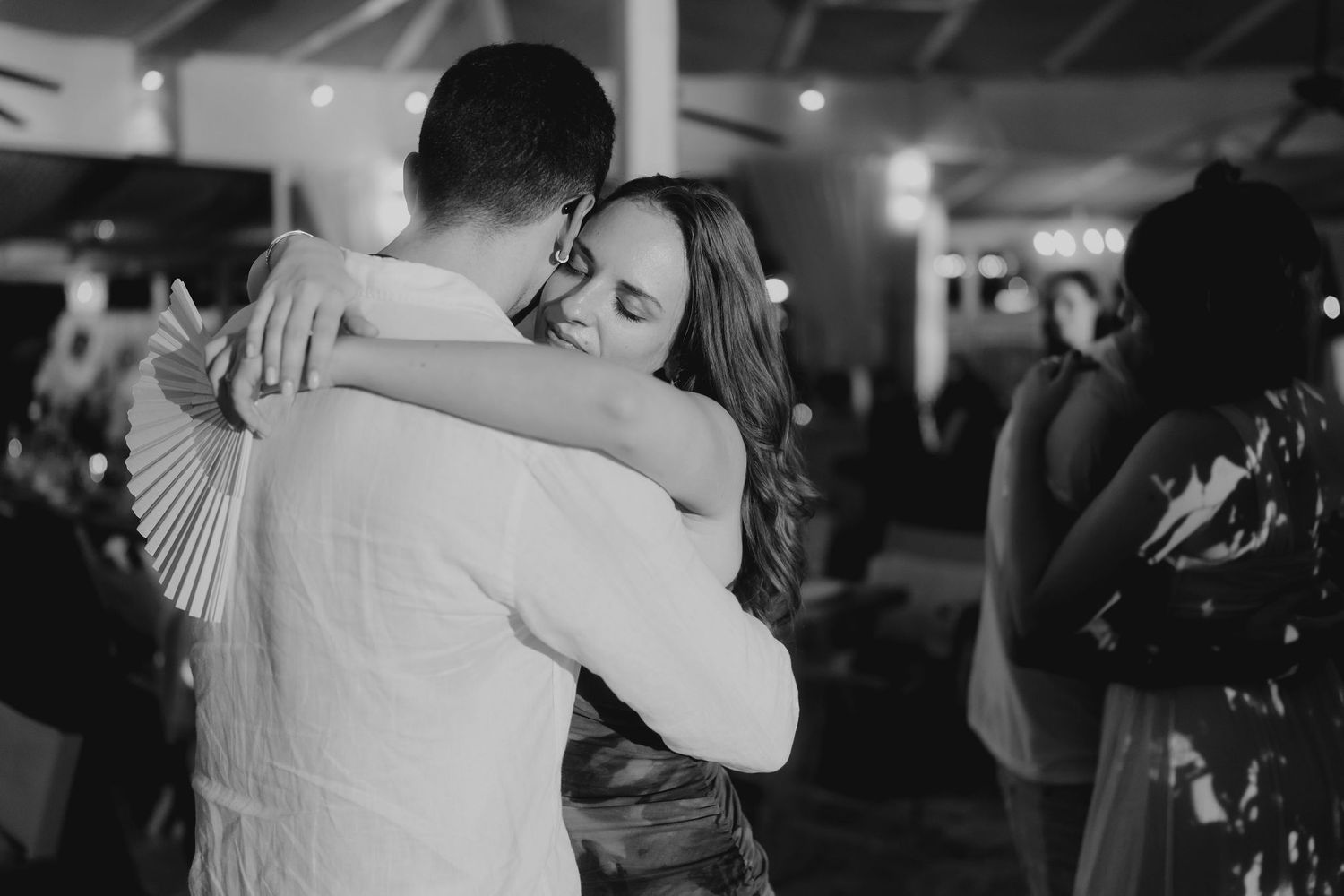 Black and white photo of a couple sharing an emotional embrace on the dance floor at a wedding reception.