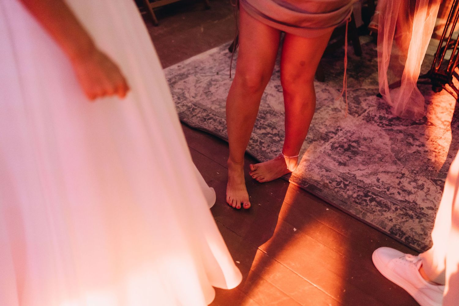 Close-up of wedding guests feet on wooden dance floor, bride in white gown visible at a reception celebration.
