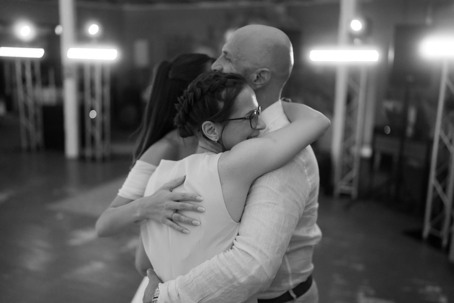 Black and white photo of a bald man and woman sharing a tender embrace on a dance floor at an event.