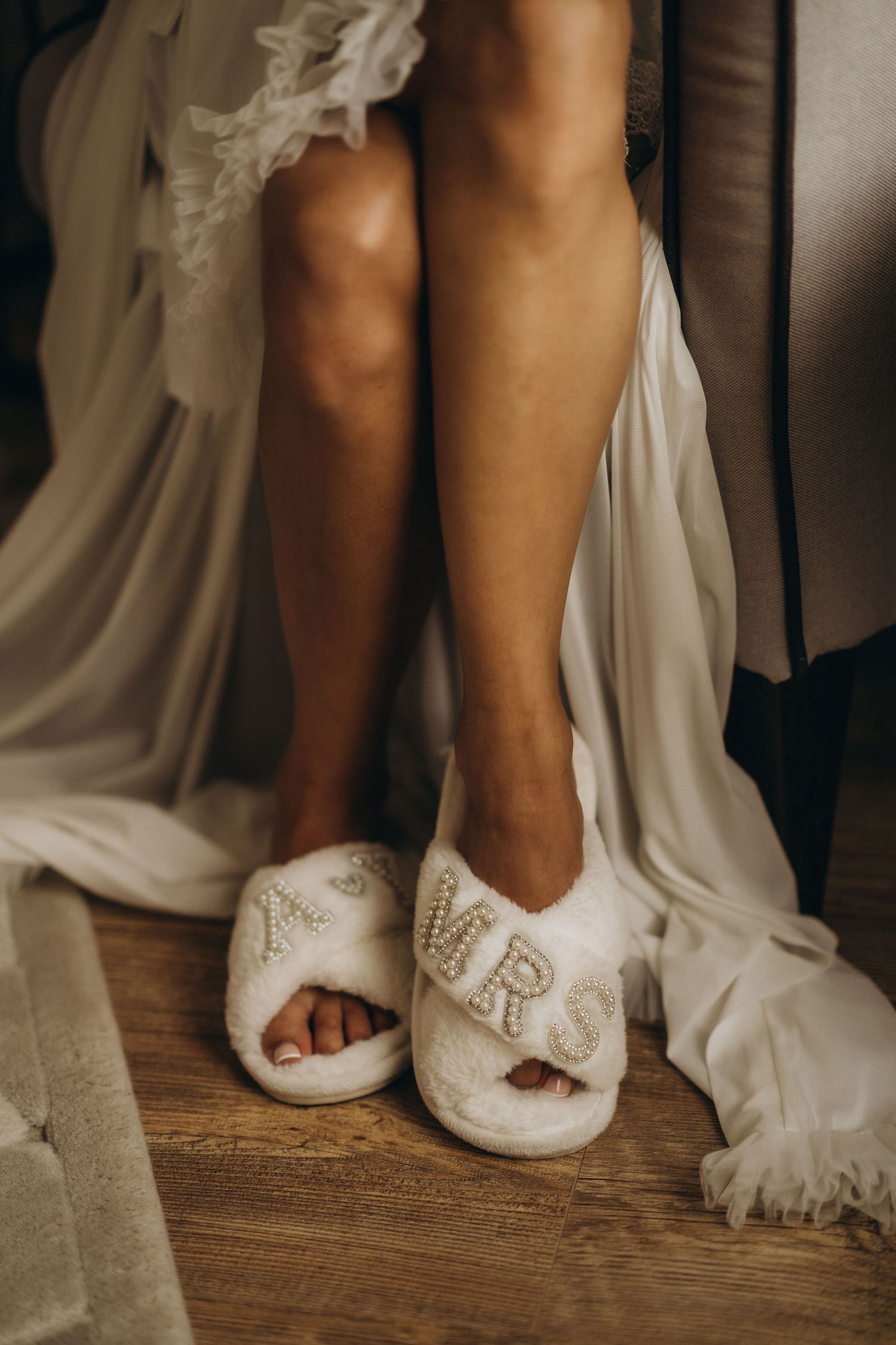 Bride wearing fluffy white MRS slippers with pearl lettering on a wooden floor in a wedding dress.