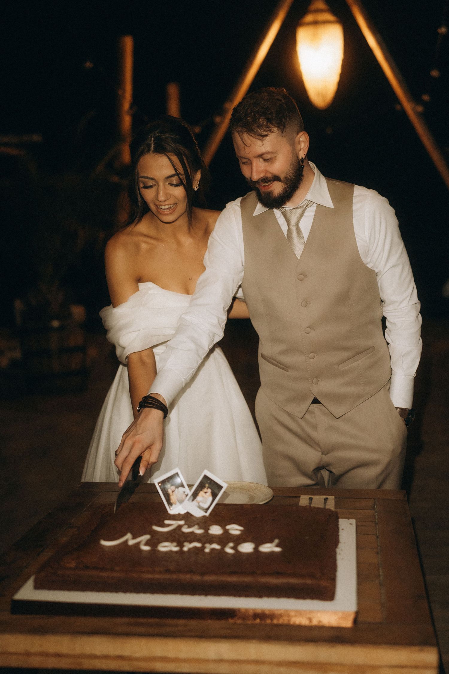 Bride and groom cutting their chocolate Just Married wedding cake together at a romantic evening reception.