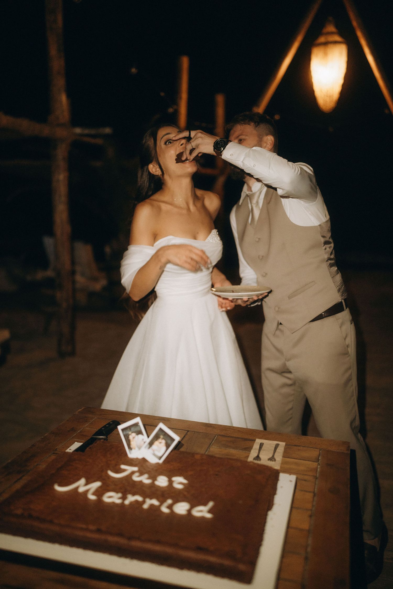 Bride and groom eating wedding cake together at night, with a Just Married cake in the foreground.