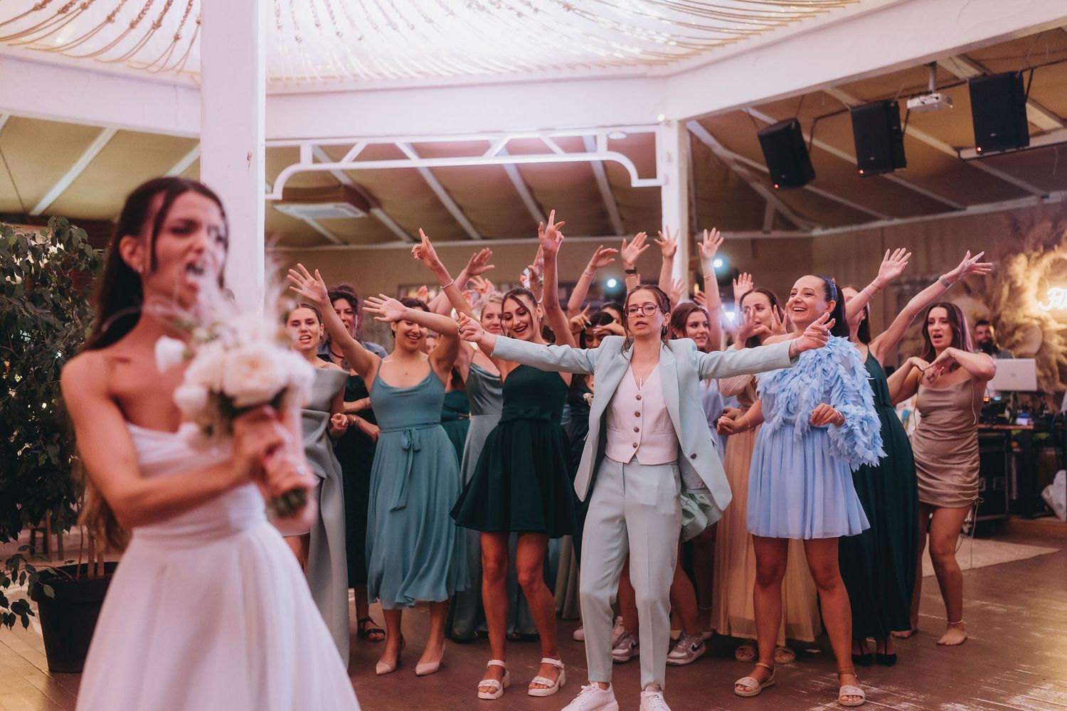 Bride tossing bouquet to excited group of wedding guests in elegant venue.