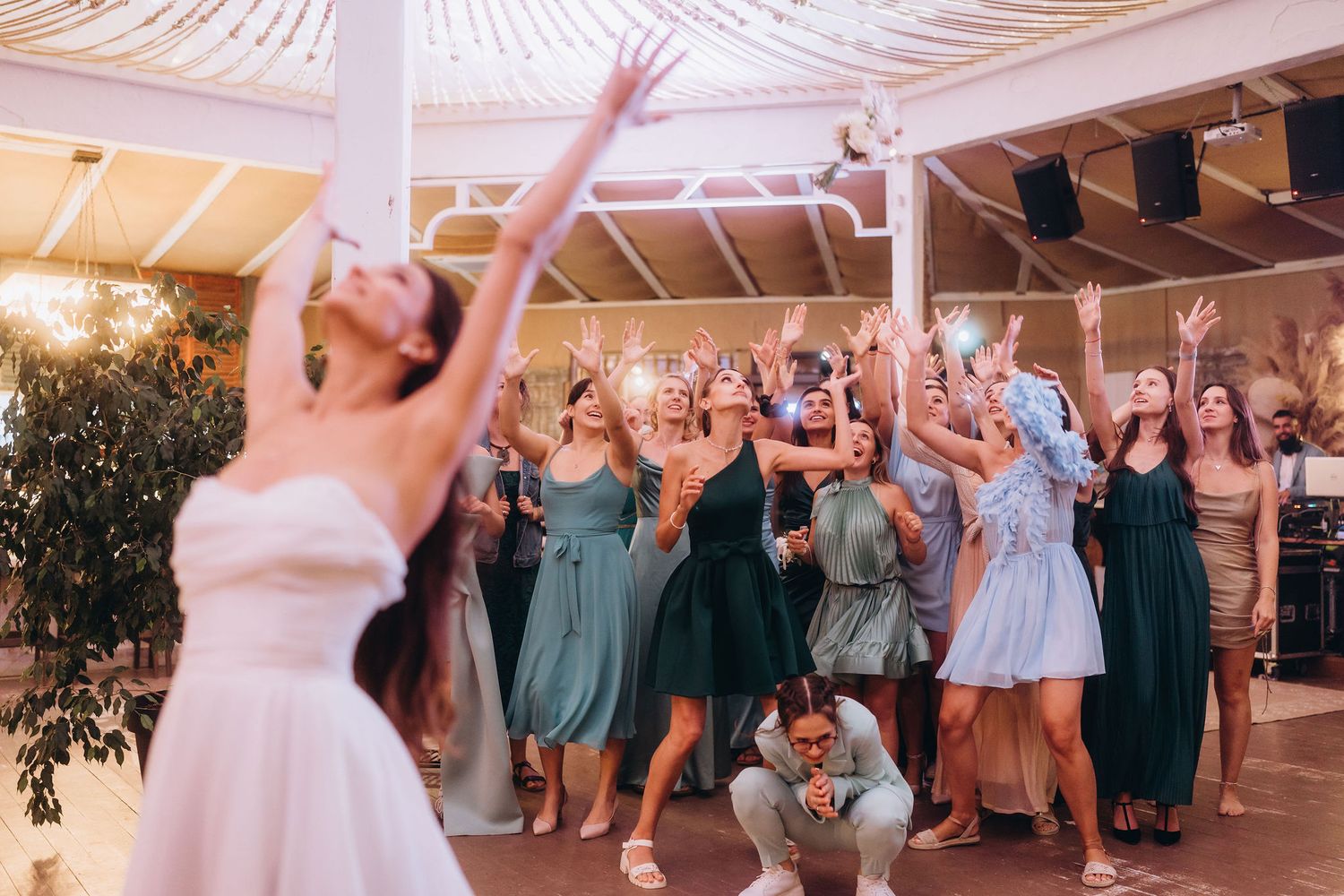 Bride tosses bouquet to excited wedding guests reaching up with hands in elegant venue.