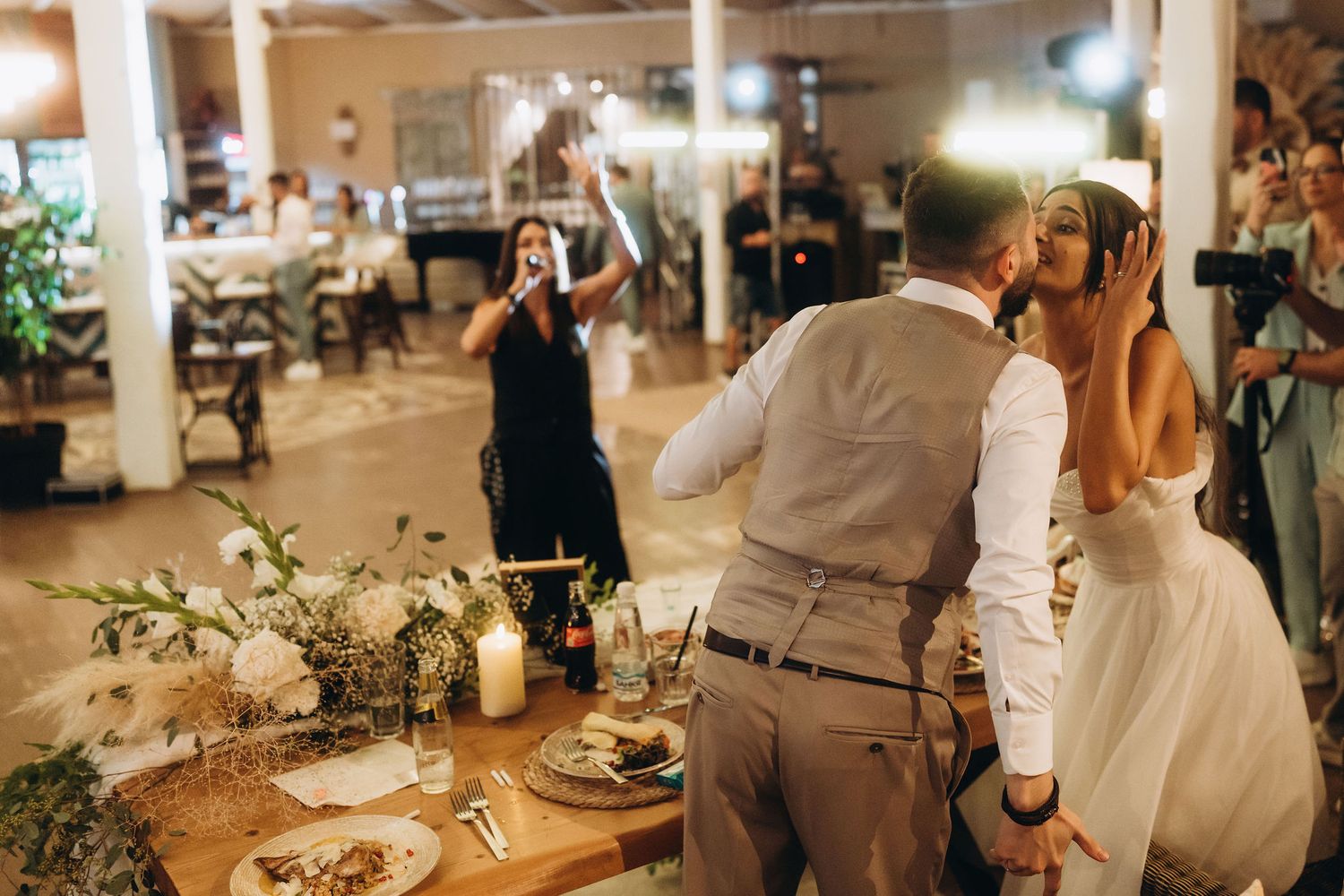Bride and groom share a tender moment during wedding reception as a singer performs nearby at an elegant venue.