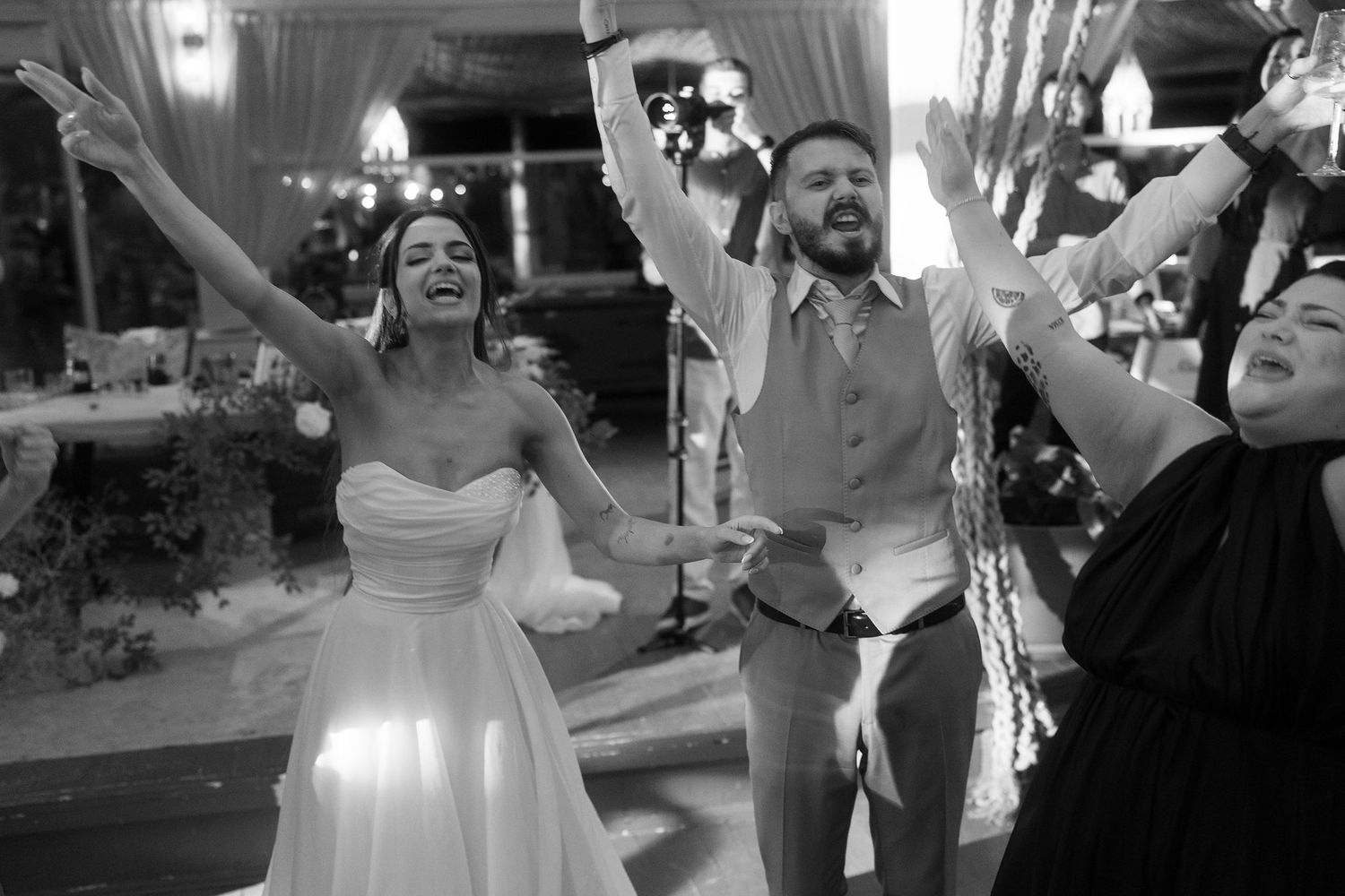 Black and white photo of a joyful bride and groom celebrating at their wedding reception with guests cheering.