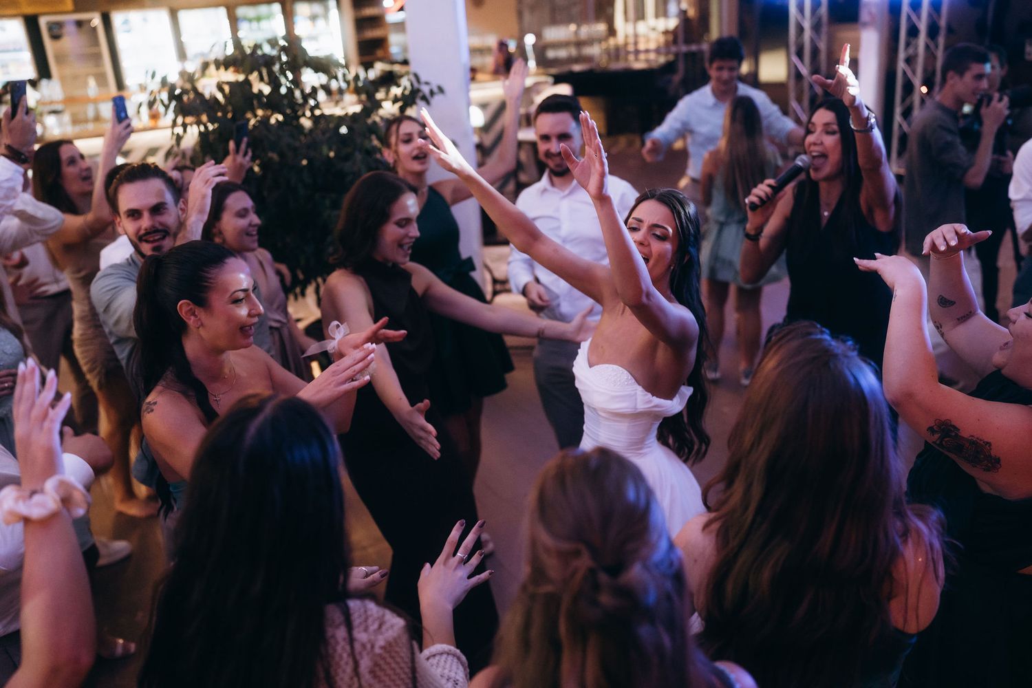 Bride and groom celebrate with guests on a lively wedding reception dance floor, surrounded by cheering friends.