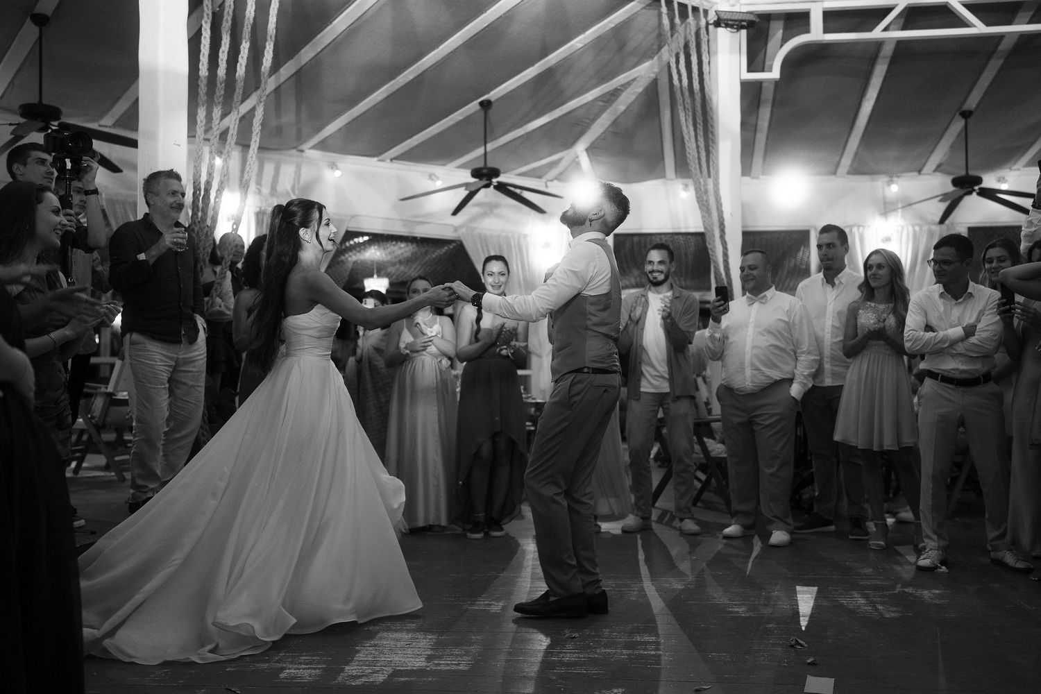 Bride and groom share a romantic first dance surrounded by wedding guests in black and white.