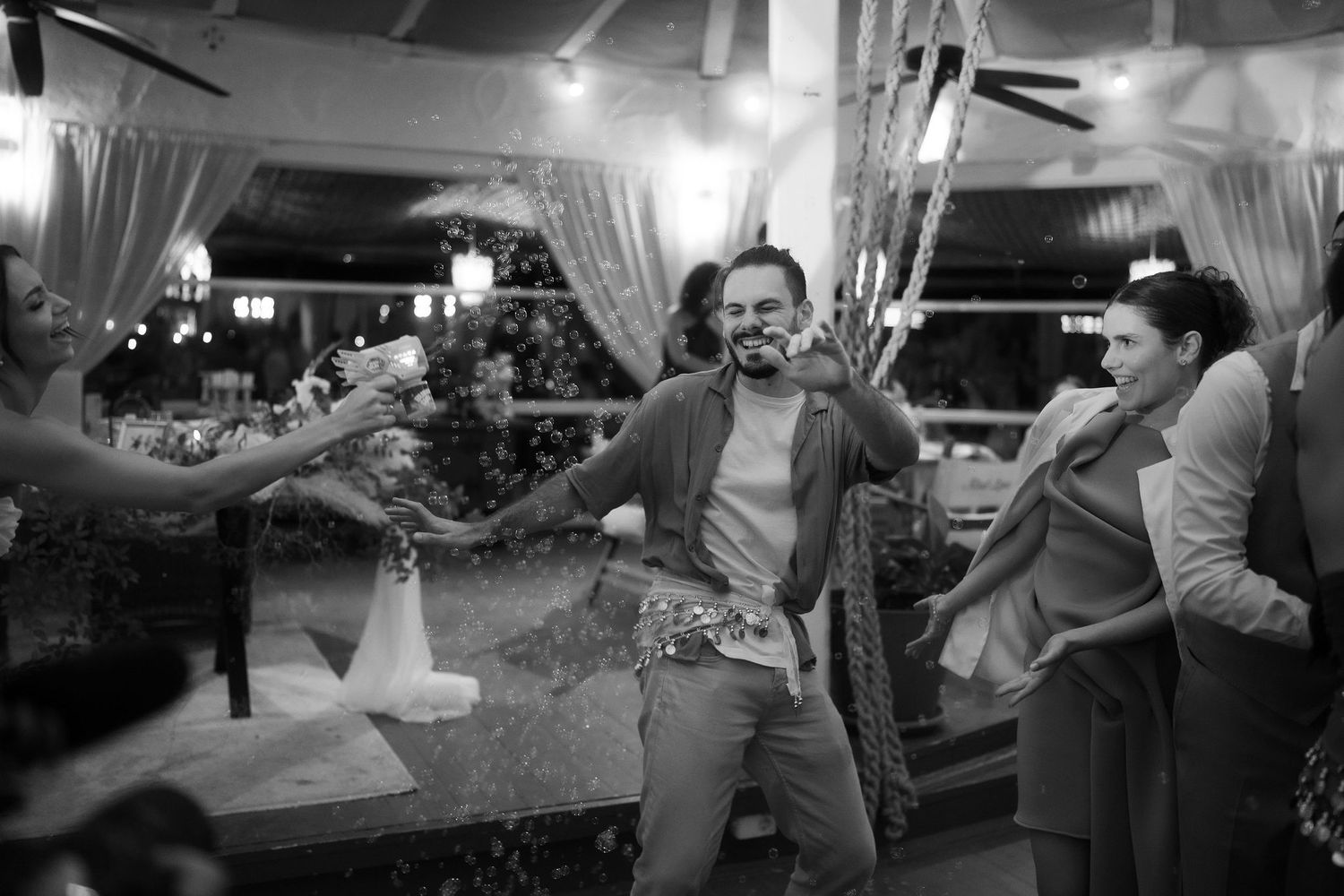 Black and white photo of a man celebrating at a party, surrounded by guests spraying champagne indoors.