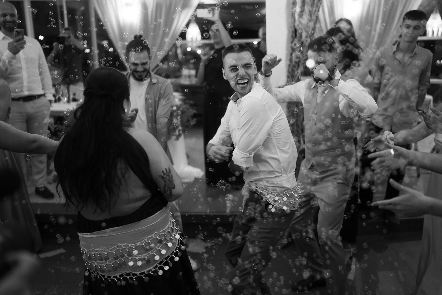Black and white photo of guests dancing and celebrating joyfully at a lively wedding reception party.